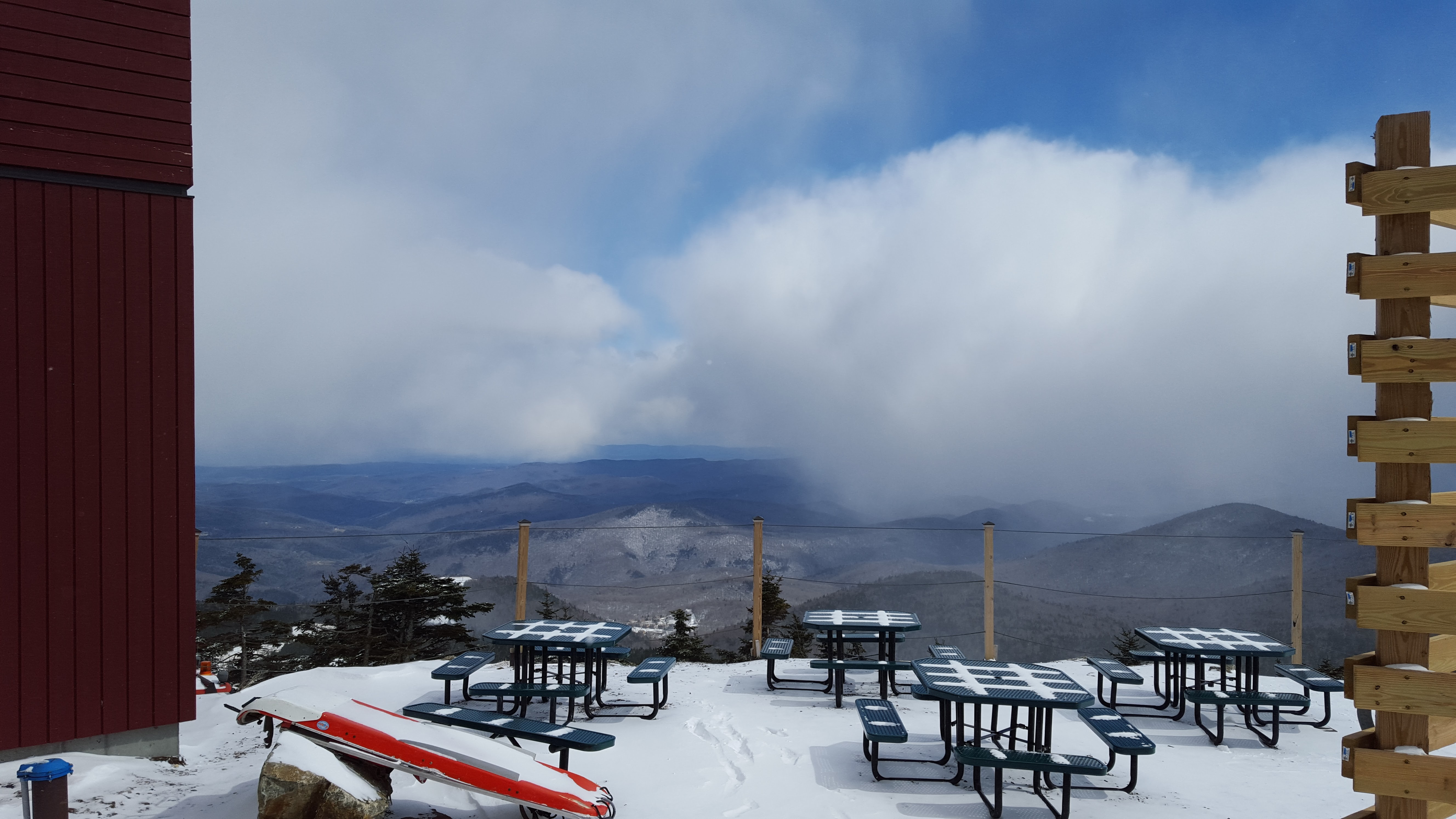 a view of mountains with clouds behind outdoor picnic tables at a mid-mountain lodge