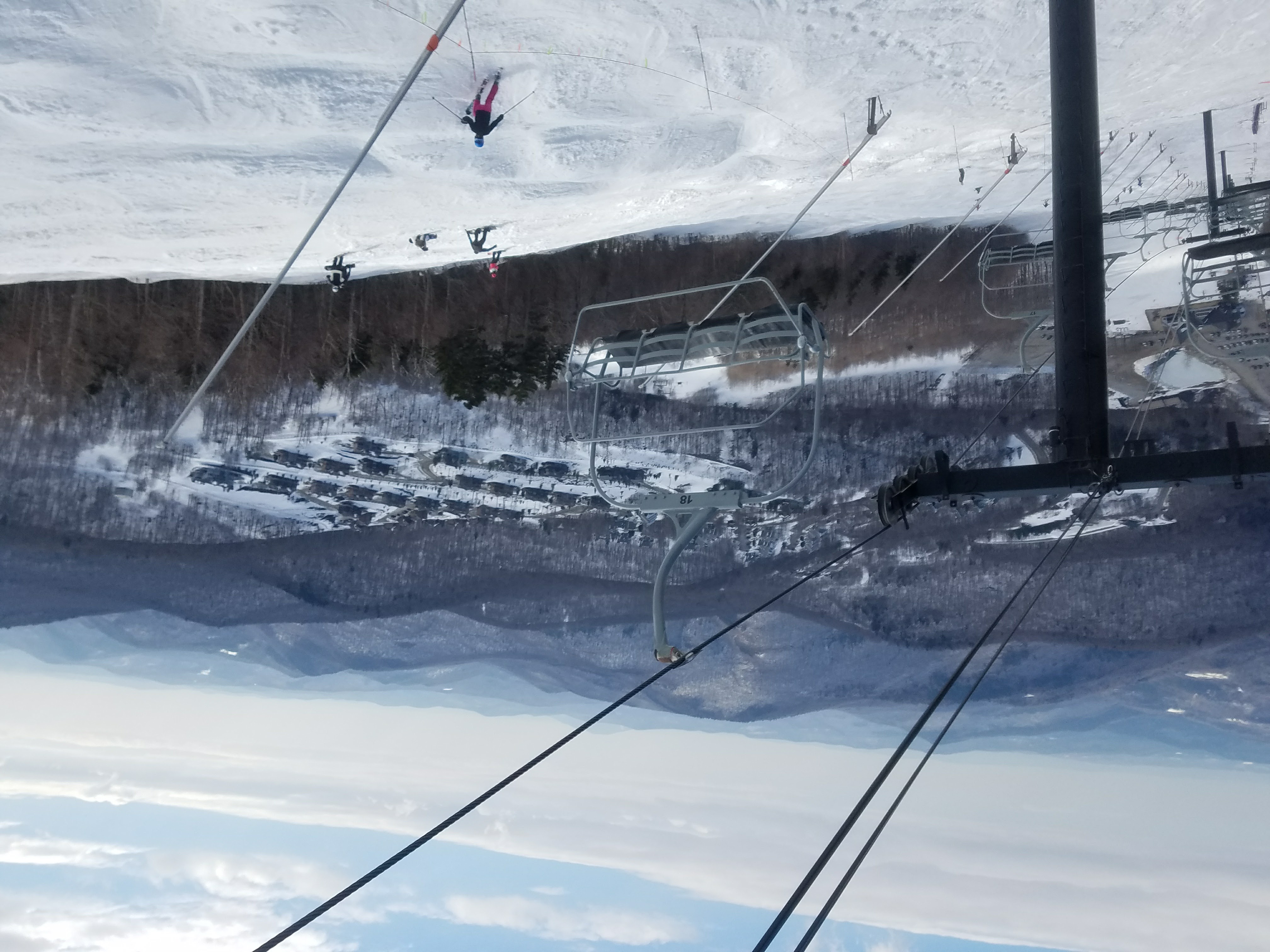 view looking down from a chairlift, the Superstar Express Quadwith skiers on a trail and mountains in the background